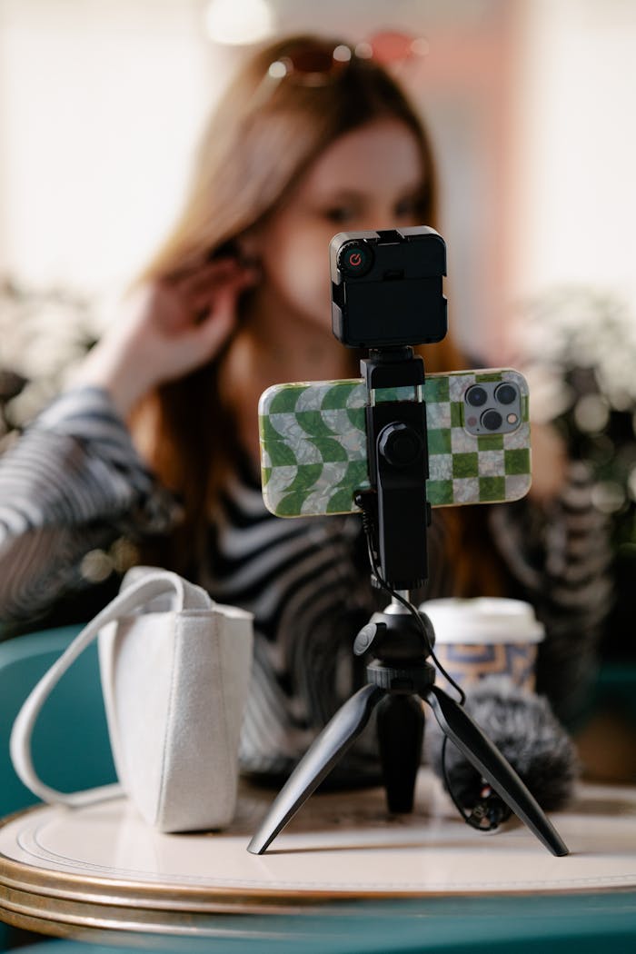 Young woman vlogging with a smartphone on a tripod, focusing on creating engaging content indoors.