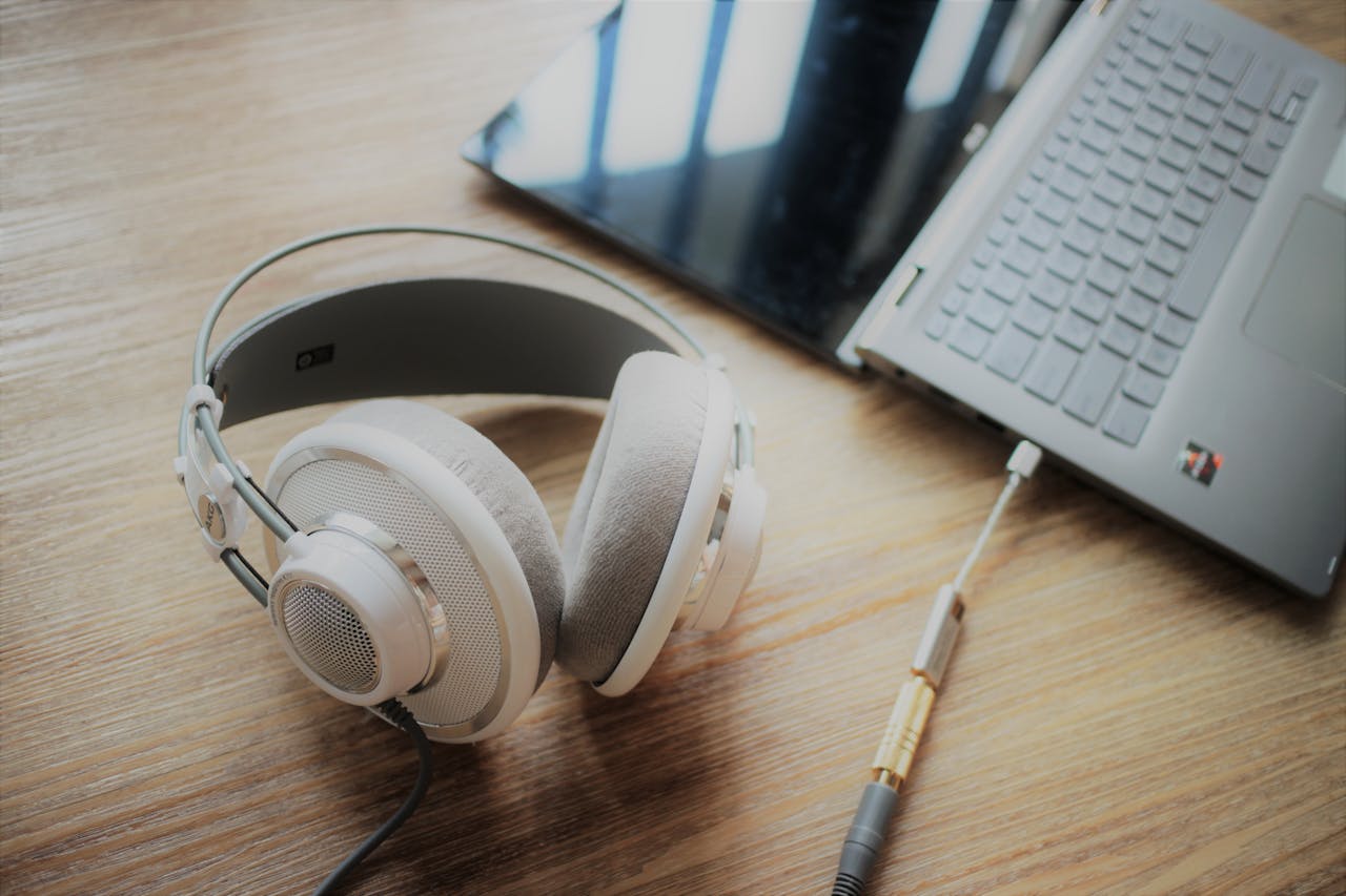 Close-up of elegant over-ear headphones connected to a sleek laptop on wooden surface, highlighting modern technology.
