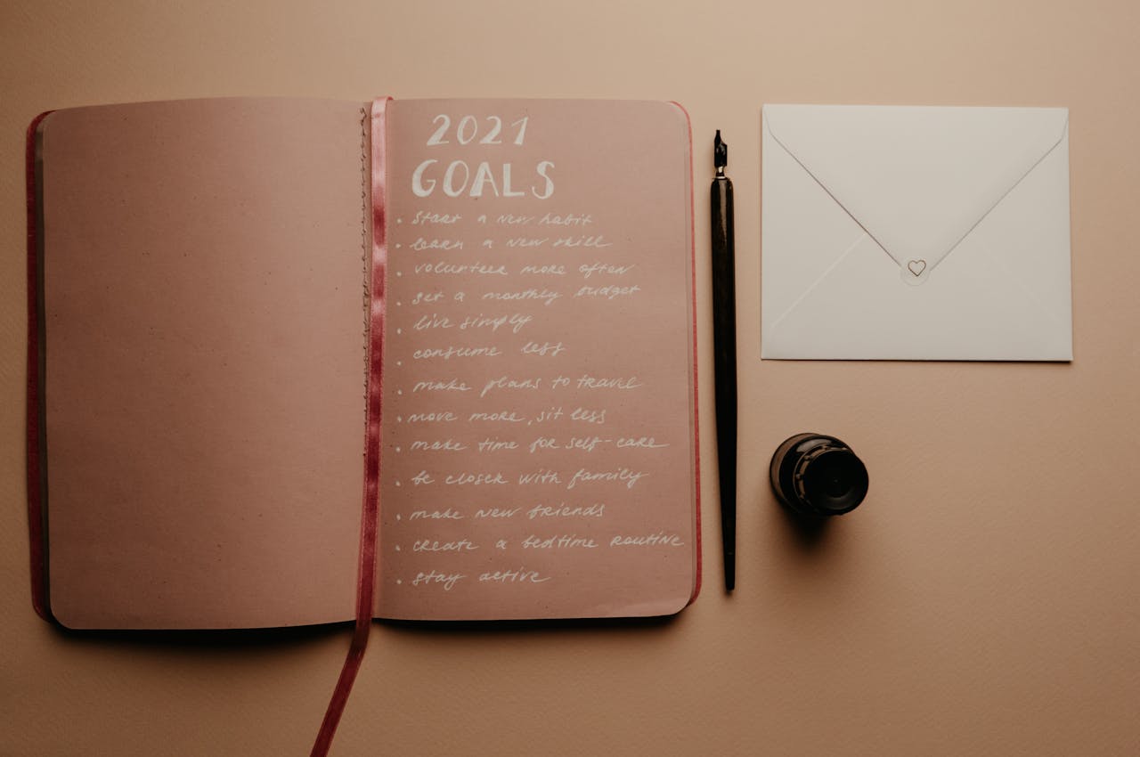 Open notebook with 2021 goals, calligraphy pen, envelope, and ink jar on neutral background.